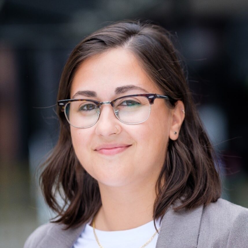 Irma Berardi wearing a light grey blazer and white shirt, smiling to camera in an outdoor setting